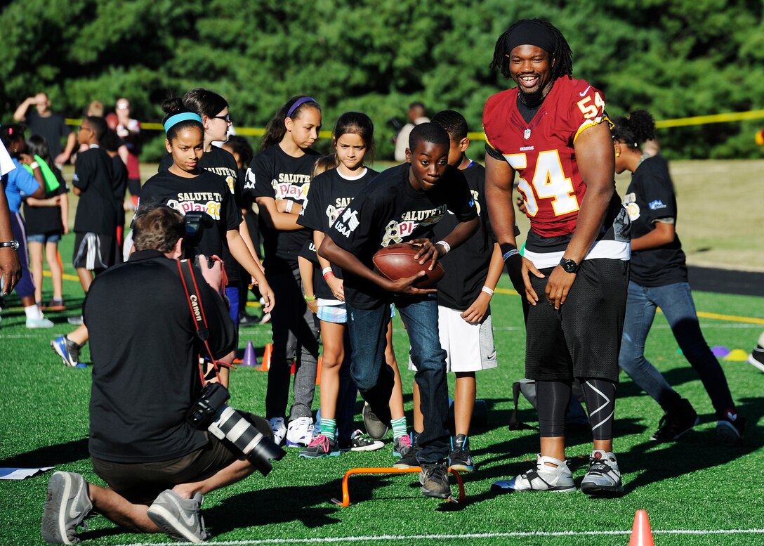 Washington Redskins linebacker Darryl Tapp assists in a football drill during the Salute to Play 60 Military Challenge at Joint Base Andrews, Md., Sept. 24, 2013. The initiative is part of the National Football League’s larger Play 60 campaign, which is designed to encourage kids to be active for 60 minutes a day to help reverse the trend of childhood obesity. (U.S. Air Force photo/ Airman 1st Class Nesha Humes)