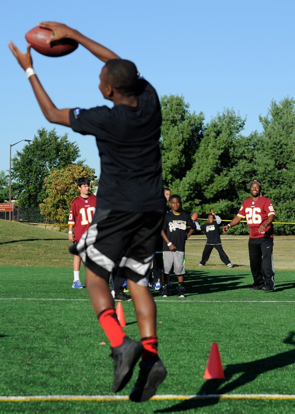 Washington Redskins cornerback Jason Wilson throws a football to a military child during the Salute to Play 60 Military Challenge at Joint Base Andrews, Md., Sept. 24, 2013. Play 60 kick-started a challenge encouraging hundreds of military families in the National Capital Region to track daily activity for four weeks. At the conclusion of the challenge the children with the highest level of participation will be recognized by the Washington Redskins organization. (U.S. Air Force photo/ Airman 1st Class Nesha Humes)