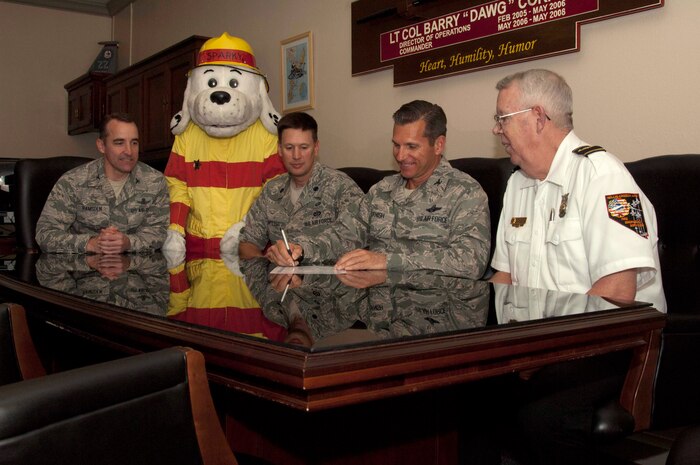 U.S. Air Force Col. Barry Cornish, 99th Air Base Wing commander, signs a Fire Prevention Week Proclamation Sept. 24, 2013, for Oct. 6 - 12 while Col. Robert Ramsden, 99th ABW vice commander; Lt. Col. Brian Hartless, 99th Civil Engineer Squadron commander; Bill Lonsford, 99th CES assistant fire chief and Sparky the fire dog, look on at Nellis Air Force Base Nev. The 2013 Fire Prevention Week theme is “prevent kitchen fires”.  According to the Center for Disease Control and Prevention cooking is the primary cause of residential fires. (U.S. Air Force photo by Airman 1st Class Timothy Young)