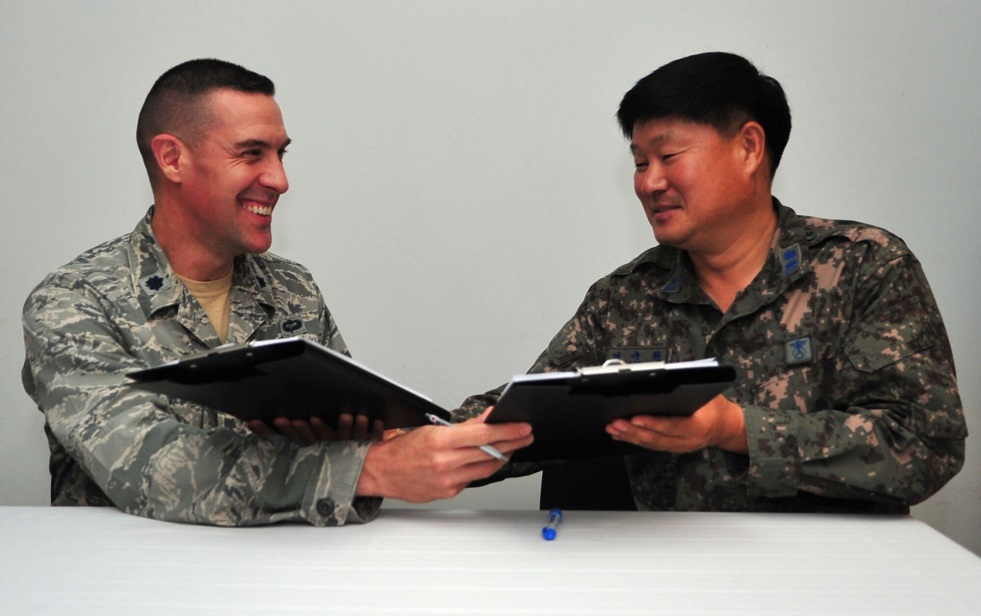 Lt. Col. Jason Beck, 51st Security Forces Squadron commander, and Republic of Korea air force Lt. Col. Gyu Hwan Lee, Military Police Squadron commander, trade copies of the Air Force and ROKAF Agreement for Base Security and Law Enforcement while signing them on Osan Air Base, ROK, Sept. 24, 2013. The document ensures both squadrons operate cohesively in order to perform entry control and law enforcement duties for the base. (U.S. Air Force photo/Airman 1st Class Ashley J. Thum)