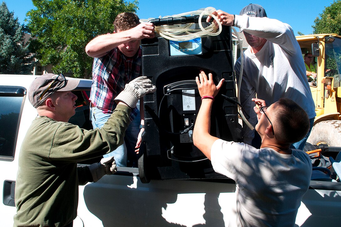 Air Force Tech. Sgt. Jessie Daughtry, lower left, Airman 1st Class Donald Neal, lower right, and Air Force Maj. Darrel Johnson, upper right, help Jamie McVaney unload a dehumidifier from his truck in Longmont, Colo., Sept. 21, 2013. Daughtry is assigned to the 90th Missile Wing, Neal is assigned to the 90th Civil Engineer Squadron and Johnson is the command post director of the 90th Missile Wing.