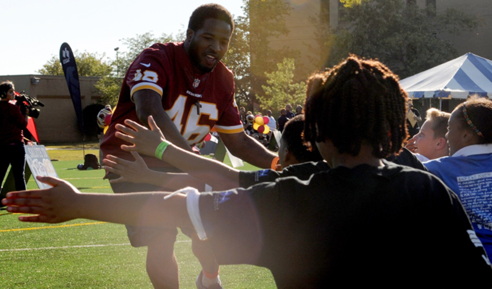 Washington Redskins running back Alford Morris high-fives children as he is introduced during the Salute to Play 60 Military Challenge Sept. 24, 2013, at Joint Base Andrews, Md. During the challenge, Redskins players and celebrity trainers lead the children through stations that included passing drills, agility ladders, 40-yard dash and a lesson on health eating habits.