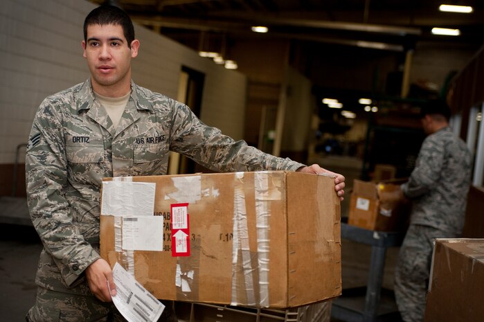 Senior Airman Donovan Ortiz, 99th Logistics Readiness Squadron outbound cargo traffic management journeyman, carries a package to a table for inspection Sept. 27, 2013, received at Nellis Air Force Base, Nev. Airmen who work with outbound cargo conduct an in-checking process to ensure cargo is properly prepared. In-checking consists of packing, processing, and moving cargo. (U.S. Air Force photo by Staff Sgt. Christopher Hubenthal)