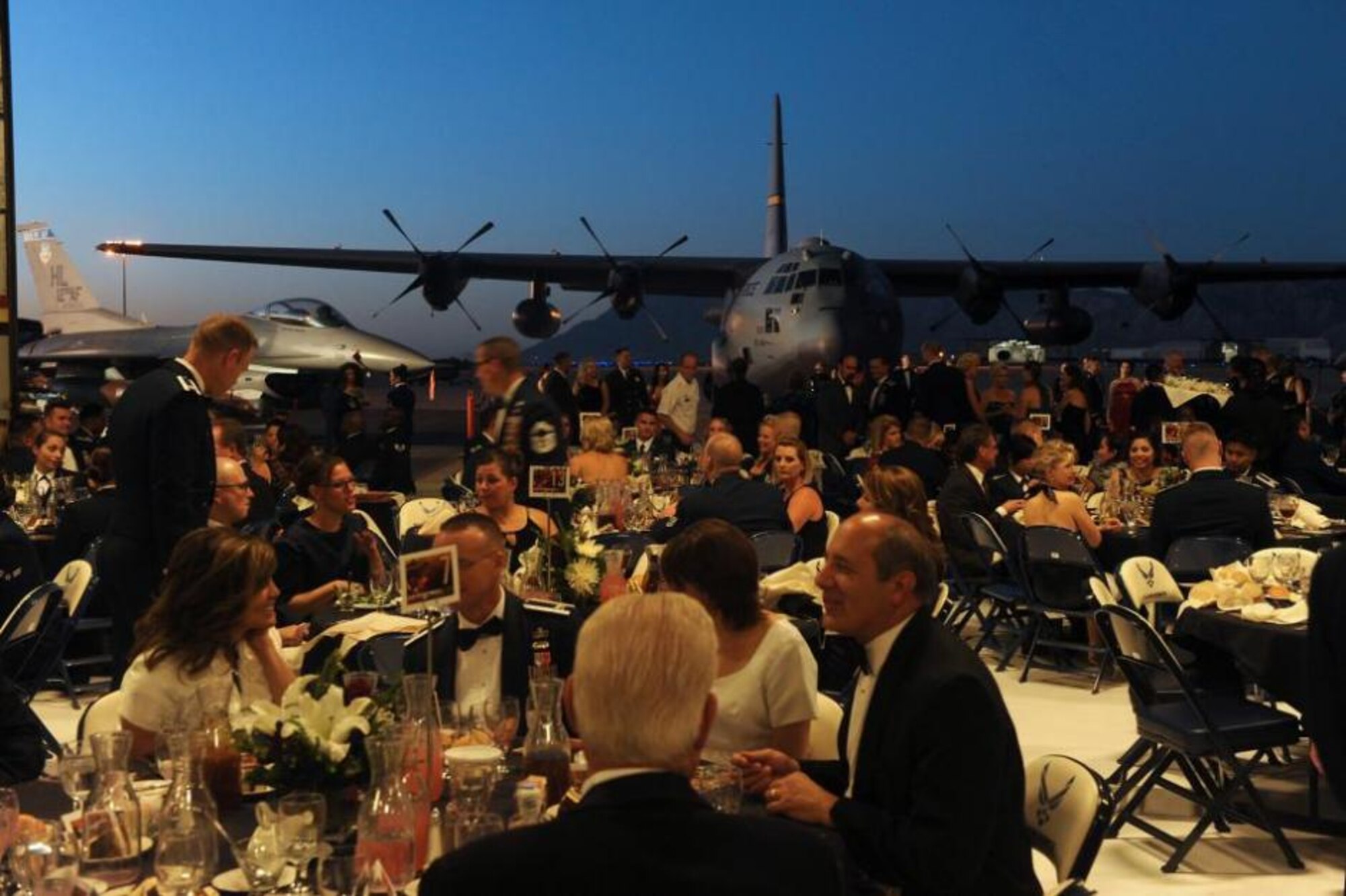An F-16 Fighting Falcon and C-130 Hercules sit outside the open hangar doors as attendees at the Air Force Ball at Hill Air Force Base, Utah, socialize at the event Sept. 20. The 23rd Utah National Guard Band provided music for the 66th anniversary celebration. (U.S. Air Force photo by Alex R. Lloyd/Released)