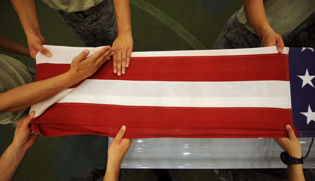 Senior Airman Christopher Bovill, 28th Maintenance Squadron Non-Destructive Inspection laboratory technician, instructs Ellsworth Honor Guard trainees on properly folding the U.S. flag during an honor guard training course in the Pride Hangar at Ellsworth Air Force Base, S.D. Sept. 19, 2013. During funeral ceremonies, members of the Ellsworth Honor Guard fold the U.S. flag in honor of the fallen servicemember and present it to the servicemember’s next of kin. (U.S. Air Force photo by Airman 1st Class Rebecca Imwalle)