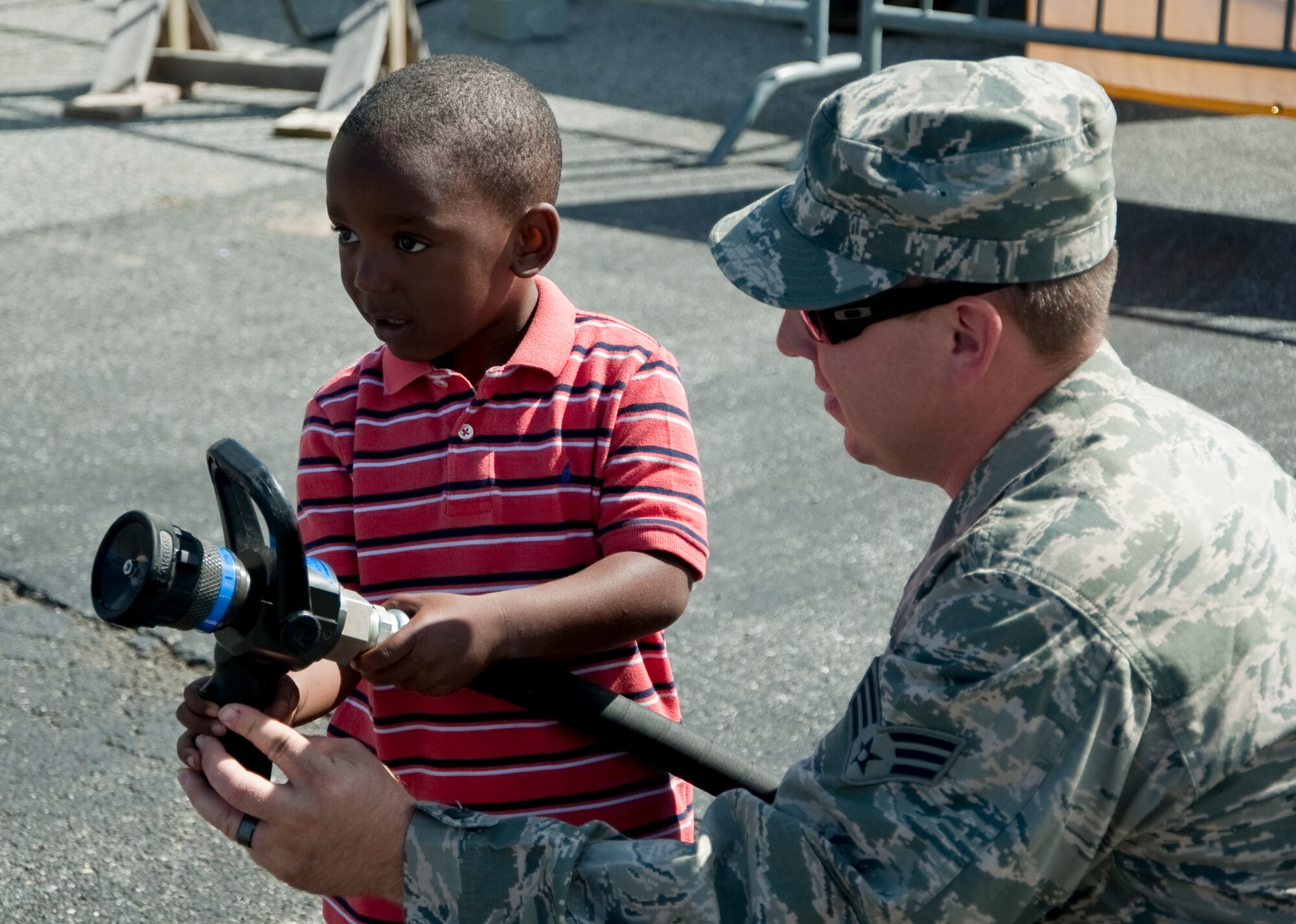 Senior Airman William Watkinson, 436th Civil Engineer Squadron firefighter, teaches Nasir Goode from Philadelphia how to hold the fire hose Sept. 29, 2013, in the Monster Fun Zone at Dover International Speedway in Dover, Del. Watkinson volunteered to show some of the tools the Dover Air Force Base firefighter use. (U.S. Air Force photo/Senior Airman Jared Duhon)