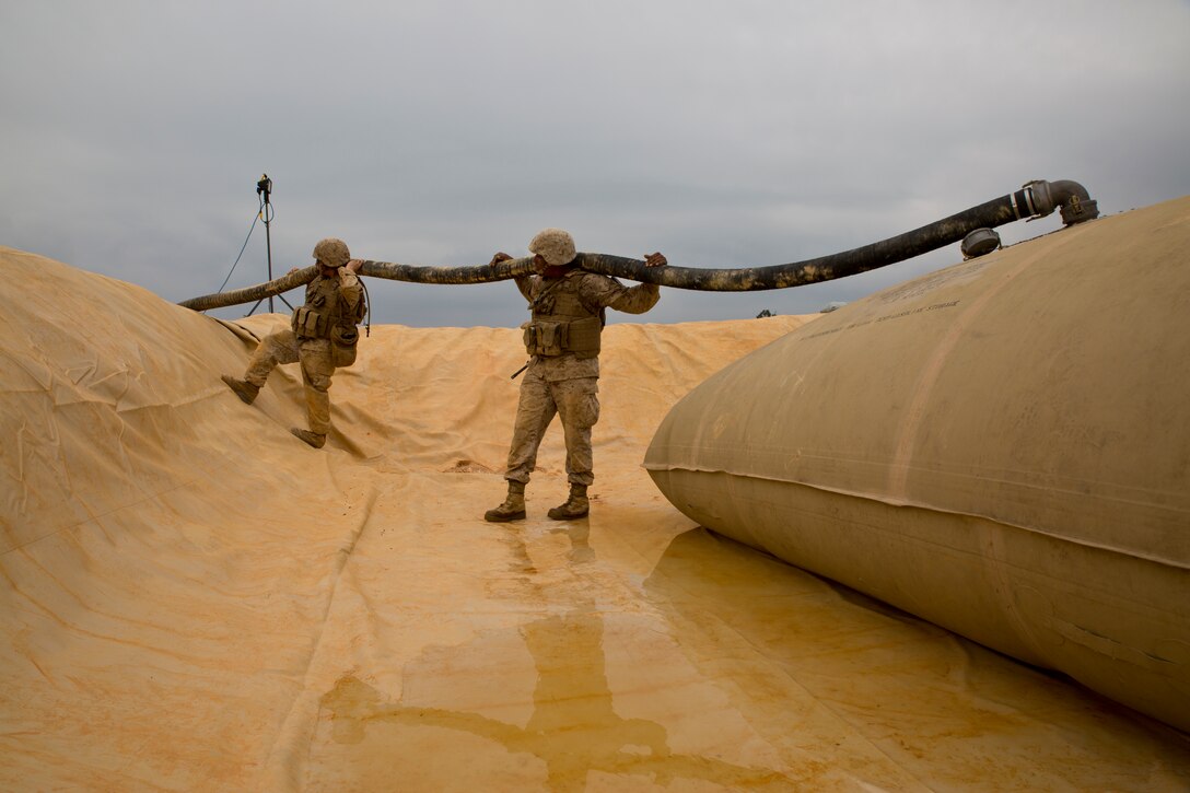 Lance Cpls. Raymond P. Sanborn, left, and Quawe M. Morgan hold up a 4-by-50 suction hose at Landing Zone Falcon in the Central Training Area March 27 during a field training exercise. Elevating the hose removes possible kinks in the fuel line and allows fuel to flow more efficiently into the storage bladder. Sanborn and Morgan are bulk fuel specialists with Bulk Fuel Company, 9th Engineer Support Battalion, 3rd Marine Logistics Group, III Marine Expeditionary Force. 