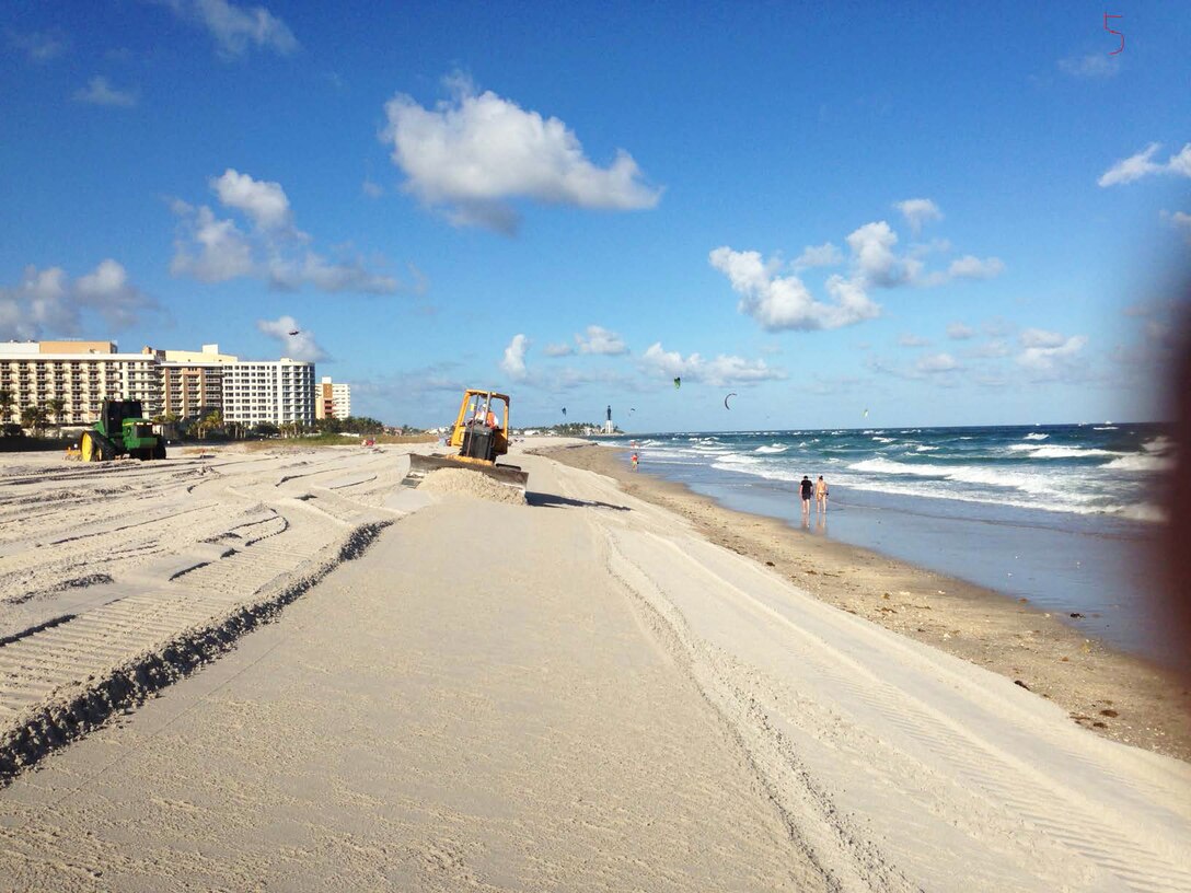 Workers flatten delivered sand on a Broward County beach so it fills an engineer-designed template, which includes the sand placement’s height and width along the beach.