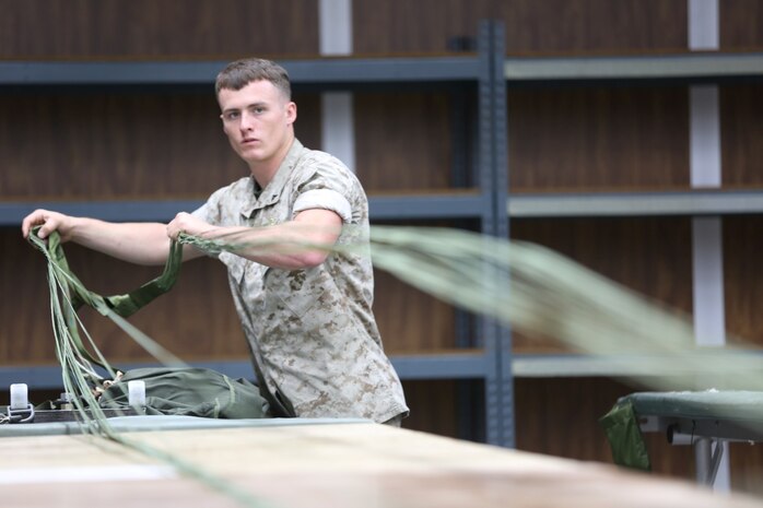 Lance Cpl. Jerrod Collier, an air delivery specialist with the platoon, Combat Logistics Regiment 17, straightens the lines of a 26-foot, high velocity parachute in preparation for inspection.  Marines with 1st ADP are responsible for packing and inspecting heavy, light and personnel parachutes used to deliver supplies by aircraft.