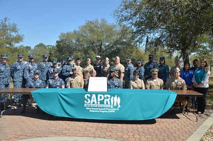 (Seated left to right)Cmdr. Patrick Boyce, Naval Consolidated Brig Charleston commanding officer, Cmdr. Shaun Murphy, Naval Operational Support Center commanding officer, Capt. Jon Fahs, Naval Nuclear Power Training Command commanding officer, Capt. Timothy Sparks, Naval Support Activity commanding officer, Capt. Marvin Jones, Naval Health Clinic Charleston commanding officer, Capt. Amy Burin, Space and Naval Warfare Systems Center Atlantic commanding officer, Cmdr. Charles Phillip, Naval Munitions Command commanding officer, and Cmdr. Victor Garza, Nuclear Power Training Unit executive officer, along with Sexual Assault Prevention and Response Victim Advocates and point of contacts along with other base leadership gather in front of building 84, April 1, 2014, to sign the Sexual Assault Awareness Proclamation. (U.S. Air Force photo/Eric Sesit)