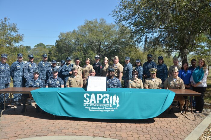 (Seated left to right)Cmdr. Patrick Boyce, Naval Consolidated Brig Charleston commanding officer, Cmdr. Shaun Murphy, Naval Operational Support Center commanding officer, Capt. Jon Fahs, Naval Nuclear Power Training Command commanding officer, Capt. Timothy Sparks, Naval Support Activity commanding officer, Capt. Marvin Jones, Naval Health Clinic Charleston commanding officer, Capt. Amy Burin, Space and Naval Warfare Systems Center Atlantic commanding officer, Cmdr. Charles Phillip, Naval Munitions Command commanding officer, and Cmdr. Victor Garza, Nuclear Power Training Unit executive officer, along with Sexual Assault Prevention and Response Victim Advocates and point of contacts along with other base leadership gather in front of building 84, April 1, 2014, to sign the Sexual Assault Awareness Proclamation. (U.S. Air Force photo/Eric Sesit)