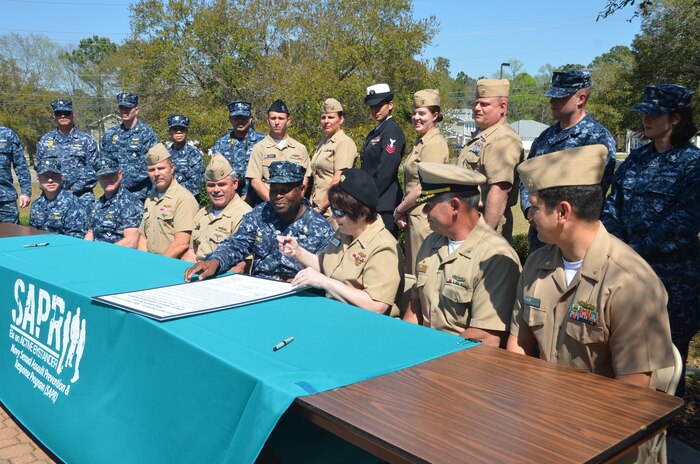 (Left to right) Cmdr. Patrick Boyce, Naval Consolidated Brig Charleston commanding officer, Cmdr. Shaun Murphy, Naval Operational Support Center commanding officer, Capt. Jon Fahs, Naval Nuclear Power Training Command commanding officer, Capt. Timothy Sparks, Naval Support Activity commanding officer, Capt. Marvin Jones, Naval Health Clinic Charleston commanding officer, Capt. Amy Burin, Space and Naval Warfare Systems Center Atlantic commanding officer, Cmdr. Charles Phillip, Naval Munitions Command commanding officer, and Cmdr. Victor Garza, Nuclear Power Training Unit executive officer, take turns signing the Sexual Assault Awareness Month Proclamation April 1, 2014, at Joint Base Charleston – Weapons Station. The proclamation states that April is Sexual Assault Awareness Month, and encourages Sailors to “Live our values: step up to stop sexual assault.” (U.S. Air Force photo/Eric Sesit)