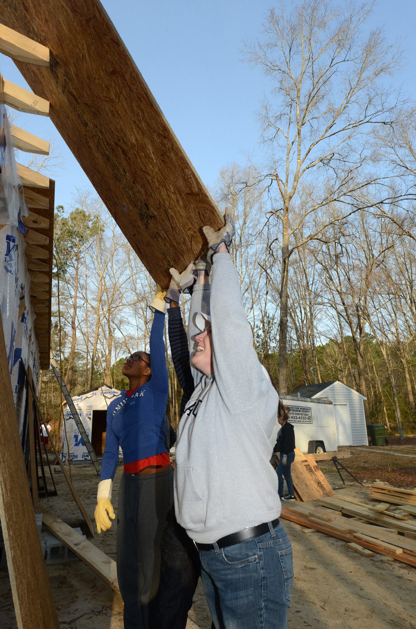 U.S. Air Force Airman 1st Class Dericka Nelson, 20th Force Support Squadron Military Personnel Flight promotions apprentice, left, and Lt. Col. Tara White, 20th FSS commander, assist with lifting a sheet of plywood onto the roof of a Kershaw County Habitat for Humanity house March 22, 2014, Camden, S.C. Airmen from the 20th FSS and the 20th Aircraft Maintenance Squadron worked on the four-bedroom house that will go to a Kershaw County family as part of a volunteer partnership between force support and the organization. (U.S. Air Force photo by Senior Airman Laura L. Valentine/Released)
