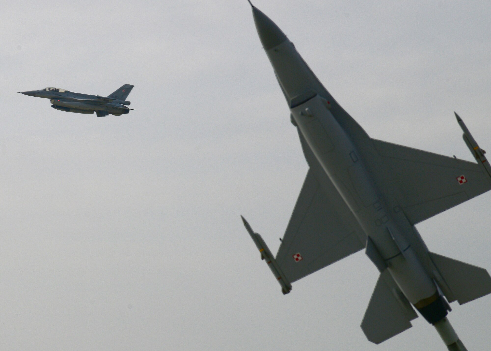 A Polish F-16 Fighting Falcon fighter aircraft passes a static display of an F-16 after takeoff, April 1, 2014, at Łask Air Base, Poland. The Polish armed forces and approximately 200 U.S. personnel have built partnership capacity together here since March 13, to increase cooperation and strengthen operational understanding of the other’s military processes, strengthening interoperability with a key NATO ally. (U.S. Air Force photo/Airman 1st Class Ryan Conroy/Released)