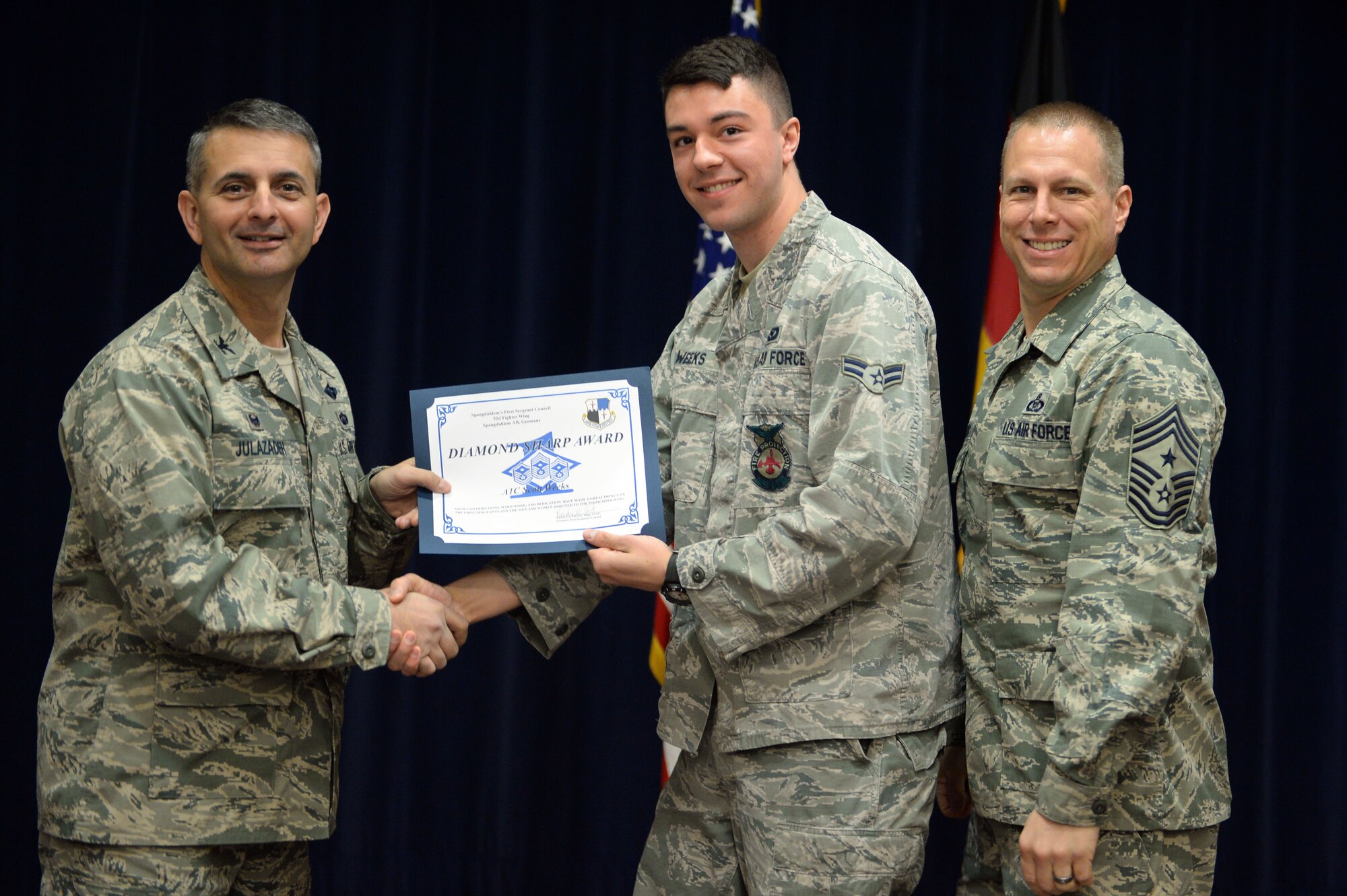 U.S. Air Force Airman 1st Class Scott Weeks, 52nd Civil Engineer Squadron firefighter from Green Bay, Wis., accepts a Diamond Sharp Award from U.S. Air Force Col. David Julazadeh, 52nd Fighter Wing commander, and U.S. Air Force Chief Master Sgt. Matt Grengs, 52nd FW command chief, right, during an awards ceremony at Club Eifel at Spangdahlem Air Base, Germany, March 31, 2014. Weeks and 16 fellow Spangdahlem Airmen received a certificate and coin as part of the First Sergeants Council’s quarterly recognition program. (U.S. Air Force photo by Senior Airman Alexis Siekert)