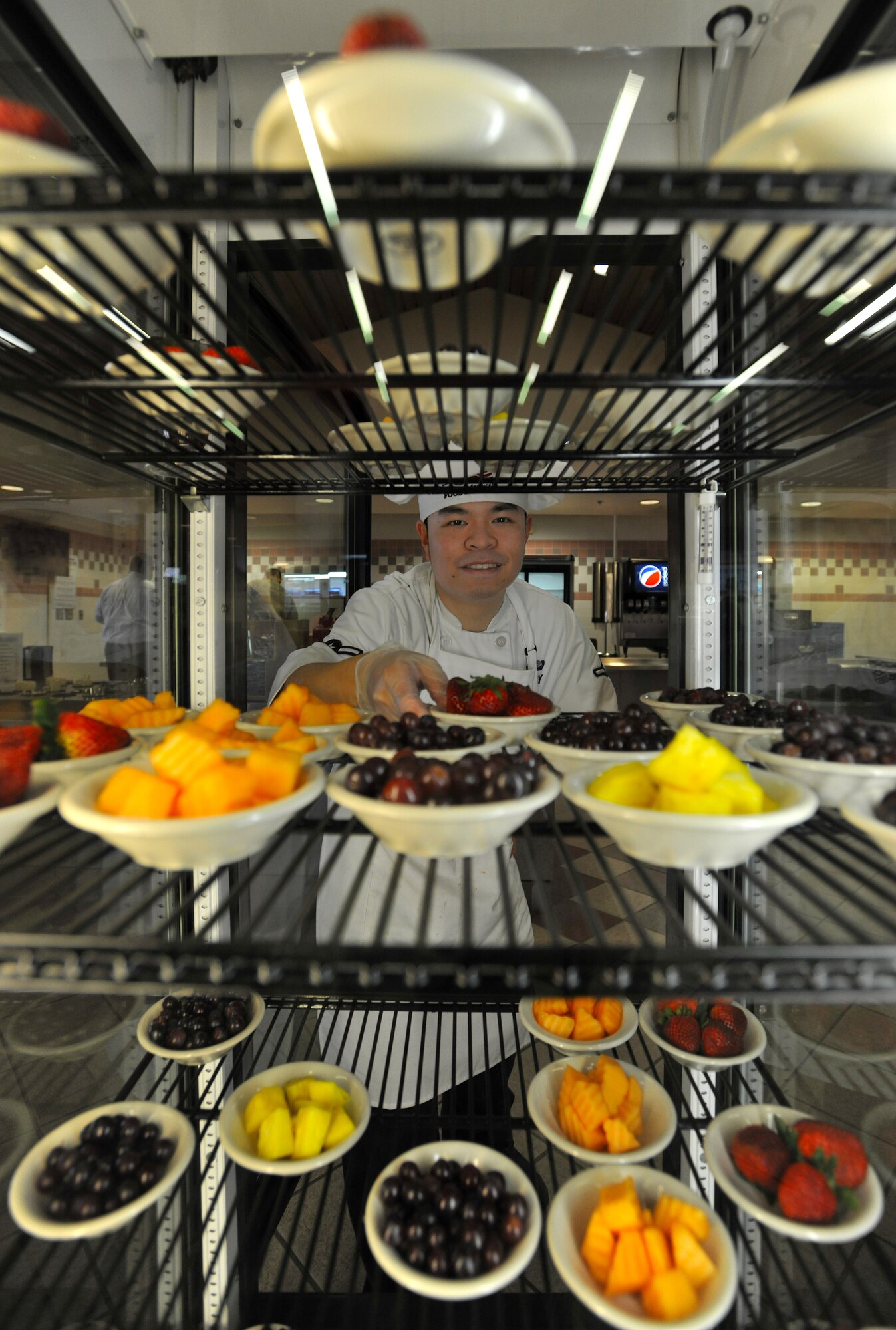 Airman Robbie Day, 319th Force Support Squadron food service apprentice, restocks the dessert fridge with fruit on March 20, 2014, at the Airey Dining Facility on Grand Forks Air Force Base, N.D. Before emigrating to the U.S. and joining the Air Force, Day was a certified chef in China, and spent most of his time cooking traditional Chinese entrees. (U.S. Air Force photo/Senior Airman Xavier Navarro)