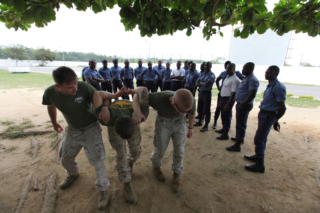 Three Marines with Special-Purpose Marine Air-Ground Task Force Africa 14.1 demonstrate how to properly escort a detainee to a group of sailors from the Ghanaian Navy during a non-lethal weapons tactics class in Takoradi, Ghana, March 19. The team of Marines demonstrated tactics that focused on the force continuum, or how to escalate the use of force for a given scenario, non-lethal ammunition and vehicle arresting devices in order to promote and strengthen the ability to conduct good governance and development.