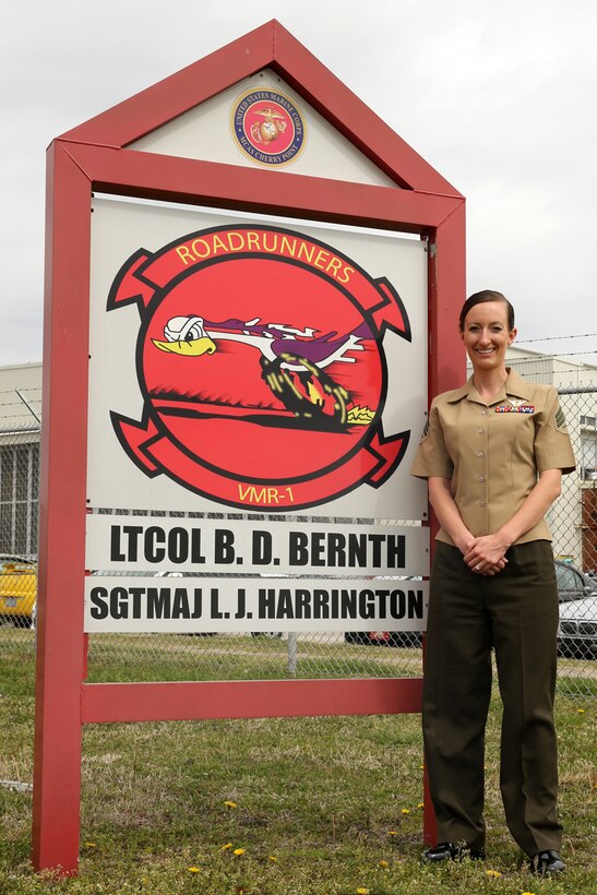 Sergeant Erica Bloomingdale, a native of Plymouth, Ohio, stands next to a sign displaying the unit logo for Marine Transport Squadron 1, March 28, 2014. Bloomingdale is a loadmaster for the VMR-1's C-9B Skytrain and the ground-training noncommissioned officer for the squadron.