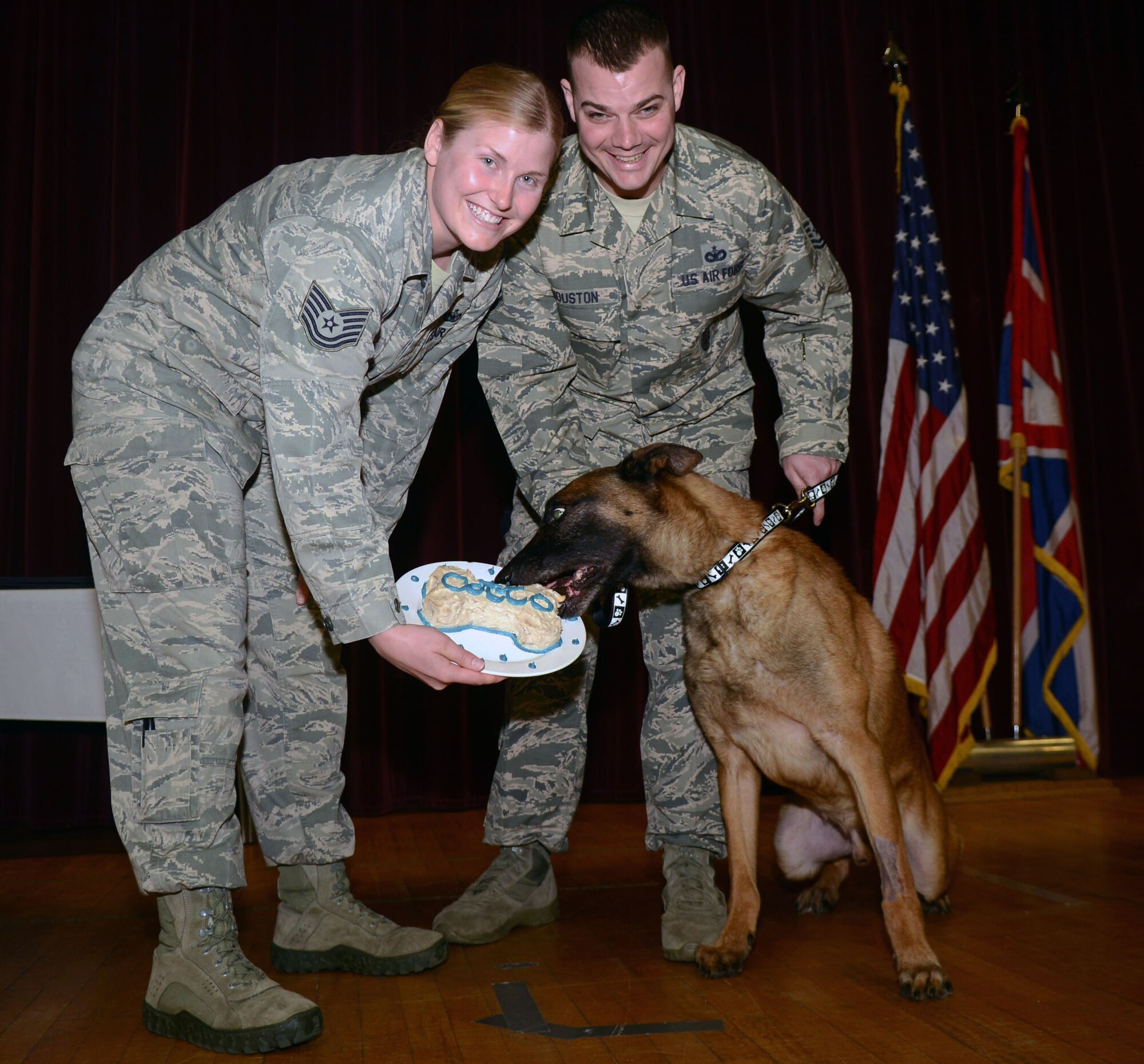 U.S. Air Force Tech. Sgt. Hannah Hobart, left, 100th Security Forces Squadron Military Working Dog kennel master from Aurora, Ind., and U.S. Air Force Tech. Sgt. John Houston, former 100th SFS Squadron MWD handler from Thibodaux, La., feed a celebratory cake to MWD Ootto after his retirement ceremony March 7, 2014, on RAF Mildenhall, England. After years of dedicated service, the MWDs have earned their retirement and respect from those in and out of uniform. (U.S. Air Force photo by Airman 1st Class Kyla Gifford/Released) 