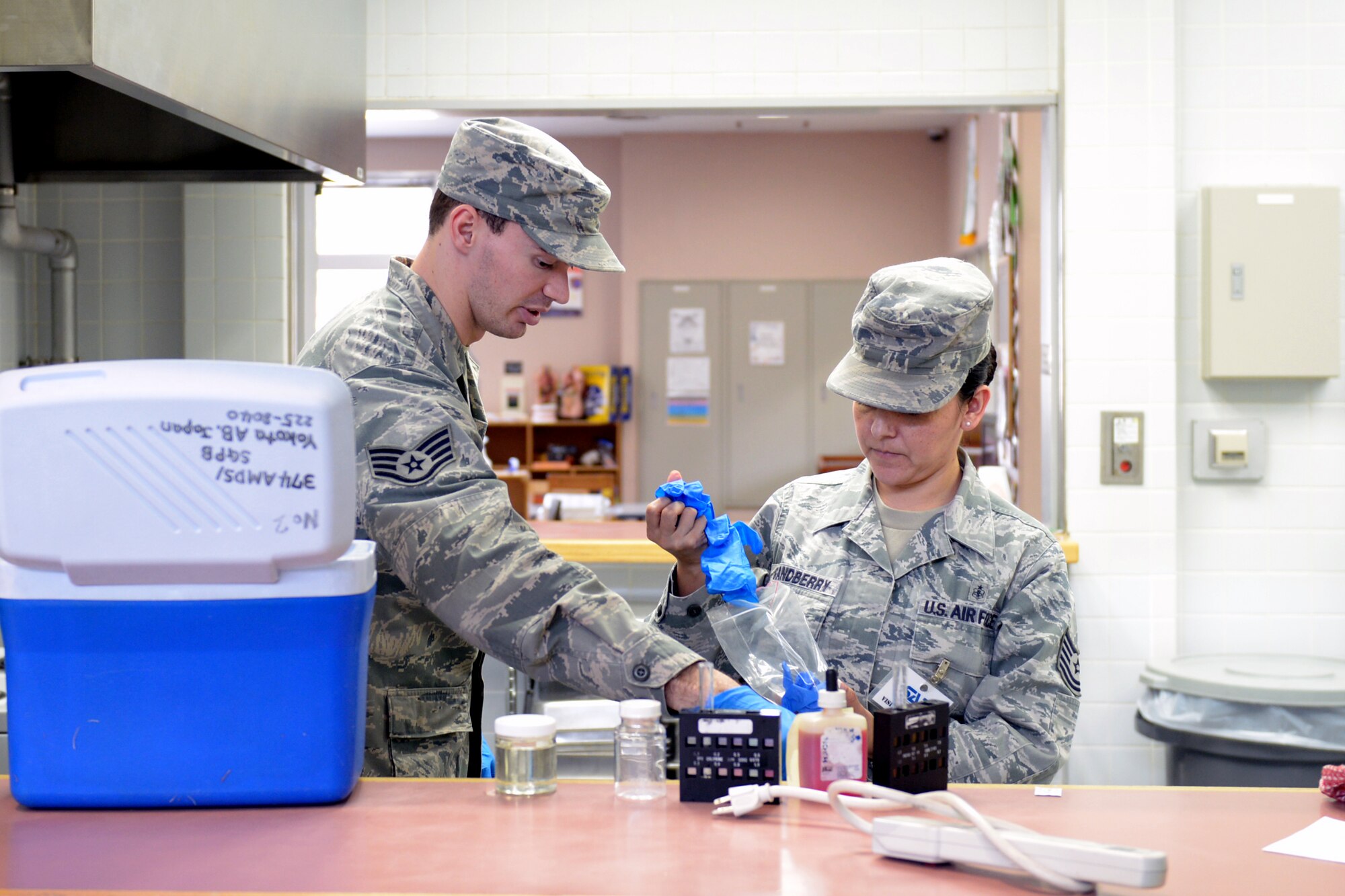 Staff Sgt. Wesley Barlow, 374th Aerospace Medicine Squadron noncommissioned officer in charge of environmental protection, and Tech. Sgt. Norma Grandberry, 374th Medical Group NCO in charge of education and training, apply personal protective equipment at Yokota Air Base, Japan, April 1, 2014. Rubber gloves prevent contamination from their skin which may cause false readings. (U.S. Air Force photo by Airman 1st Class David Danford/Released)