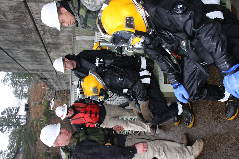 PHOTO: SGT Bryan Crowley, standing left, gives instructions to divers seated left to right, SGT Scott Wilson and PFC Kiley Bannan, while other dive team members look on, left to right, PFC Jesse Moore, SFC Blanchard Woodcox, and PFC Jordan Ramirez. 
