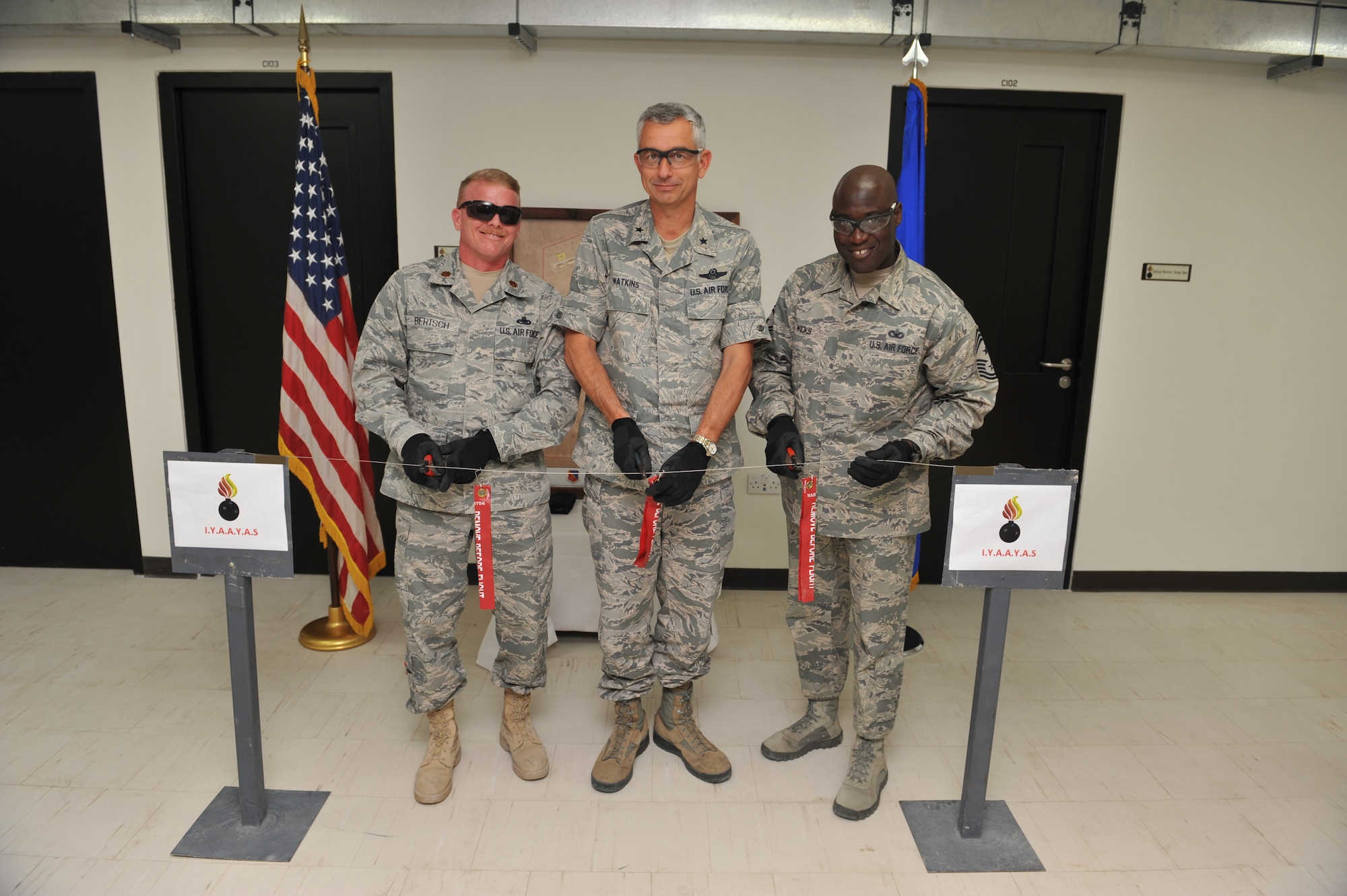 Maj. Jay Bertsch, 379th Expeditionary Maintenance Squadron commander, Brig. Gen. Roger H. Watkins, 379th Air Expeditionary Wing commander and Chief Master Sgt. Rory Wicks, 379th AEW command chief, cut an arming wire representing the formal opening of the consolidated munitions administration building at Udeid Air Base, Qatar, Mar. 31, 2014. The west munitions storage area expansion project is a $55.4 million project that began in Jan. 2011 and was recently completed, increasing operational and safety efficiencies that allows multiple organizations to work in one facility. Bertsch is serving a one year assignment and is a Lena, Ill., native. Watkins is assigned here and hails from Fort Worth, Texas. Wicks is assigned here and a Kinston, N.C., native. (U.S. Air Force photo by Master Sgt. David Miller)