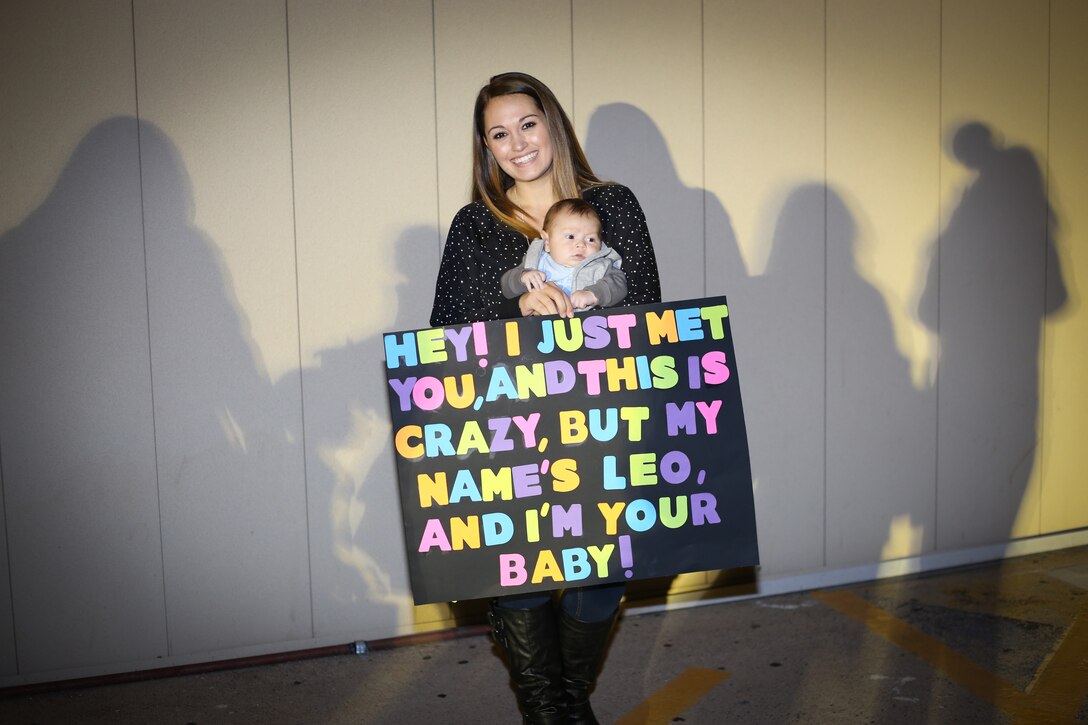 Jessica Mastorakos stands holding a sign and her son while waiting for her husband to return from deployment. Jessica regularly volunteers in order to help others overcome challenges unique to military families.