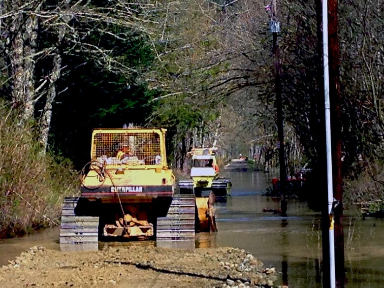 Employees with contractor Penny Lee, based out of Arlington, operate a dump truck and a D-5 bulldozer to push, smooth and compact material in 18 inches of water where the U.S. Army Corps of Engineers, Seattle District, is assisting Snohomish County with construction of a temporary berm to reduce flood impacts and prevent near-term flooding of SR 530 near mile post 37 at C Post Road.  Searchers have ongoing and planned recovery activities in this area after a March 22 mudslide constricted flow of the Stillaguamish River and caused flooding upstream.  Construction began today and the initial pass will be to match the water surface elevation with rock and embankment material and try to connect to high ground with the intention of raising it to elevation of SR530 at the berm’s completion in a week or so.  