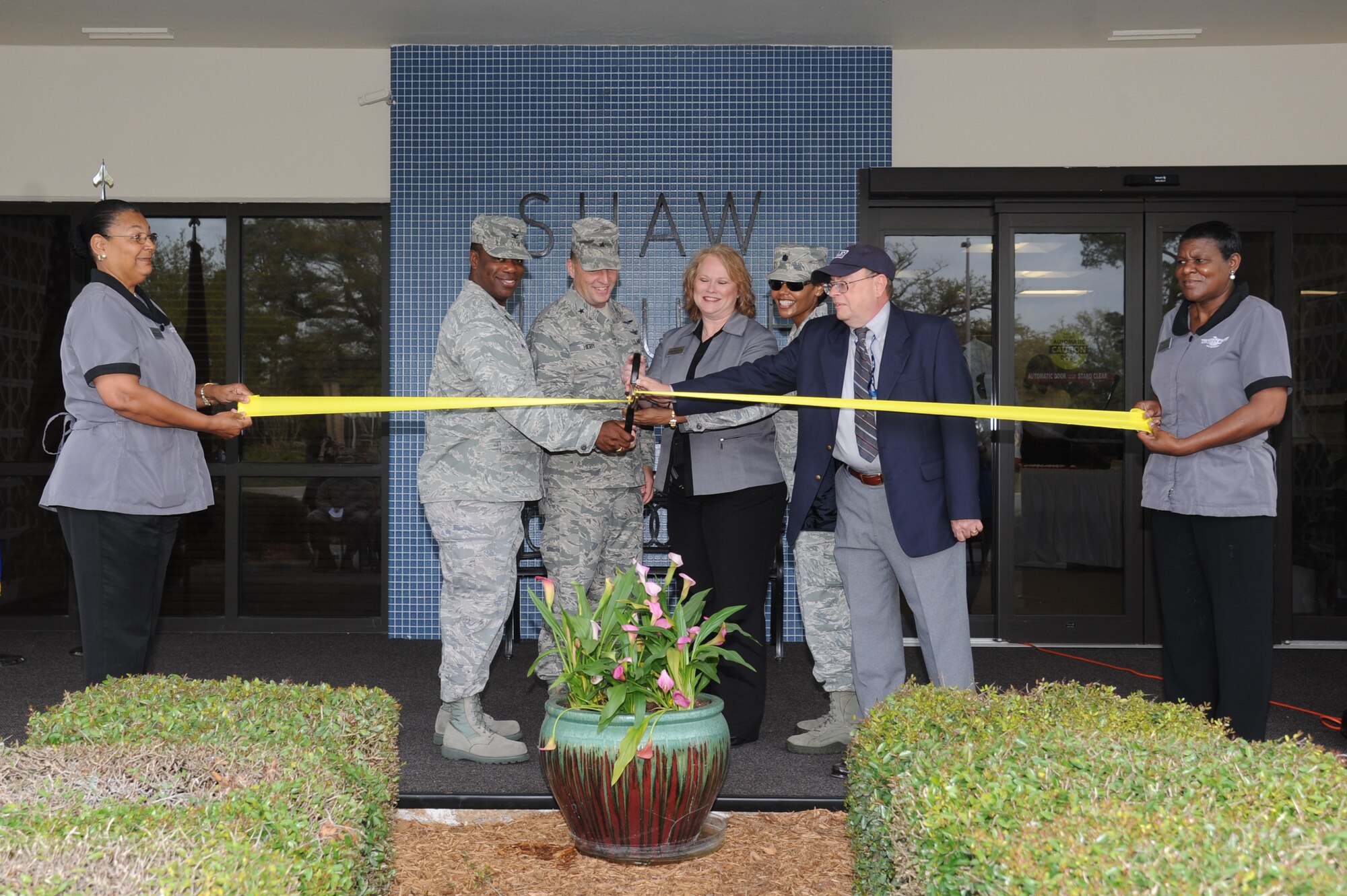 Mildred Chapman, outgoing Shaw House custodial worker supervisor, and Rosie Odom, incoming Shaw House custodial worker supervisor, hold the ribbon as it is cut by Col. Mark Vivians, 81st Mission Support Group commander; Brig. Gen. Patrick Higby, 81st Training Wing commander; Barbie Ragno, 81st Force Support Squadron Inns of Keesler general manager; Lt. Col. Sharon Nickelberry, 81st FSS commander, and Dave Horner, Pacific Architects and Engineers manager engineering construction, during the Shaw House ribbon cutting ceremony April 3, 2014, at Keesler Air Force Base, Miss.  The Shaw House facility, named after Capt. William Stevenson Shaw, was originally constructed in 1966 and last renovated in 2013.  (U.S. Air Force photo by Kemberly Groue)