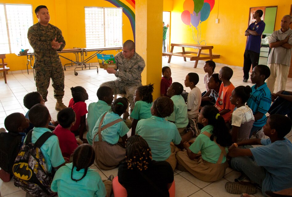 U.S. Marine Corps Cpl. Parnell Sararana, New Horizons Civil Affairs Detachment, standing left, signs to students while U.S. Air Force Staff Sgt. Jon Espinoza, New Horizons civil engineer, seated center, reads April 4, 2014, at the Stella Maris School Belize Academy for the Deaf in Belize City, Belize. Sararana started learning sign language approximately six years ago to communicate with a family member who is deaf. Spending the day with the students while deployed in support of New Horizons Belize 2014 was the first time Sararana has been able to apply his signing skills while in uniform. 