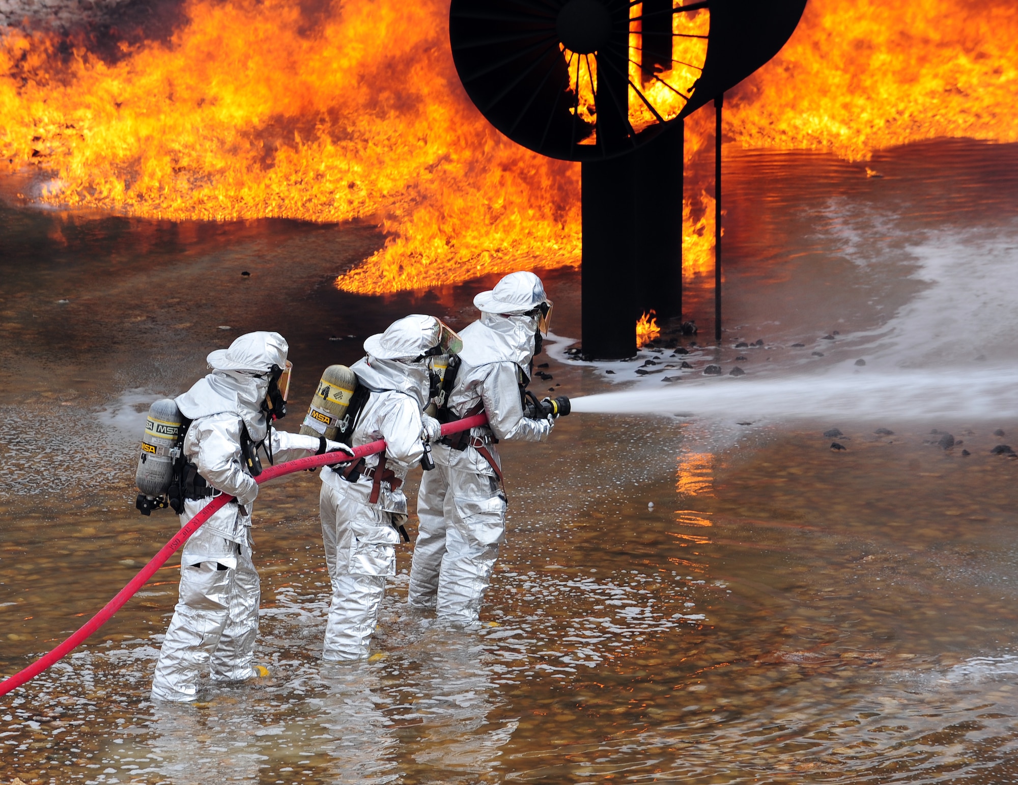 Firefighters from the 7th Civil Engineer Squadron and the Abilene Regional Airport Fire Department extinguish flames during a live fire training exercise April 2, 2014, at Dyess Air Force Base, Texas. The silver fire proximity suits that firefighters wear are manufactured from vacuum-deposited aluminized materials that designed to reflect high radiant heat produced by fire. (U.S. Air Force photo by Senior Airman Kia Atkins/Released)