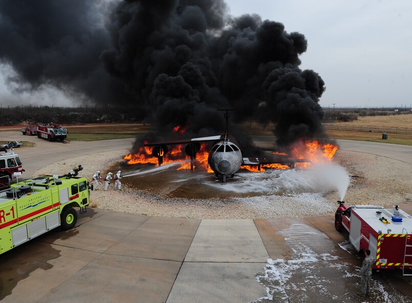 Firefighters from the 7th Civil Engineer Squadron and the Abilene Regional Airport Fire Department extinguish flames during a live fire training exercise April 2, 2014, at Dyess Air Force Base, Texas. The silver fire proximity suits that firefighters wear are manufactured from vacuum-deposited aluminized materials that designed to reflect high radiant heat produced by fire. (U.S. Air Force photo by Senior Airman Kia Atkins/Released)
