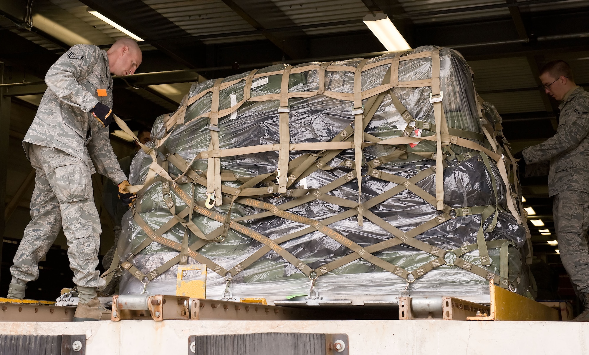 Staff Sgt. Brian Price, left, and Airman 1st Class Joshua Davison, right, both from the 436th Aerial Port Squadron, tighten web netting on a baggage pallet April 4, 2014, at the deployment processing line on Dover Air Force Base, Del. Price and Davison built baggage pallets as part of deployment line processing. (U.S. Air Force photo/Roland Balik)