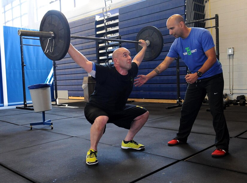 U.S. Marine Corps Gunnery Sgt. Juan Ospina, Joint Task Force Civil Support operations noncommissioned officer in charge, coaches U.S. Army Staff Sgt. David Scott, 128th Aviation Brigade combatives instructor, as he does an overhead squat during a CrossFit session held at the Anderson Field House at Fort Eustis, Va., March 21, 2014. Ospina is the JTF-CS physical training promotion coordinator and the lead Fort Eustis CrossFit instructor. He believes physical fitness enhances unit readiness by promoting team cohesion and mental alertness. (Department of Defense photo by U.S. Air Force Tech. Sgt. Gwendolyn Blakley/Released)