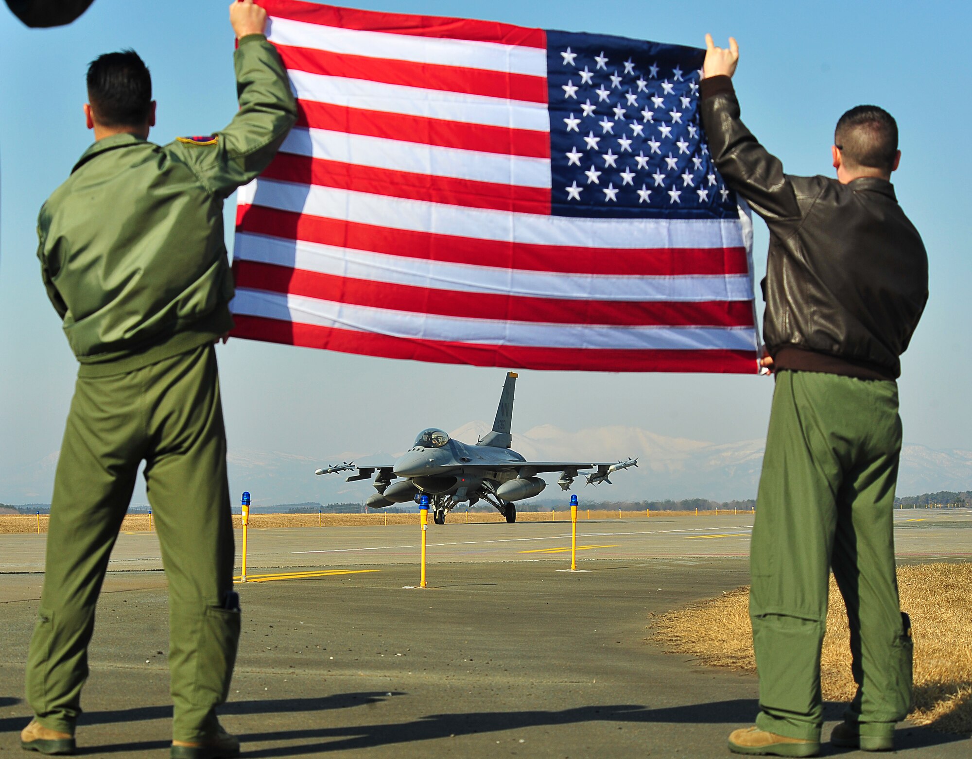 Members of the 13th Fighter Squadron lift the American Flag in show of support to their fellow pilots during an early morning fly-off of F-16 Fighting Falcons at Misawa Air Base, Japan, April 8, 2014. A fleet Wild Weasels departed for deployment in support of U.S. Air Force operations abroad. (U.S. Air Force photo/Senior Airman Jose L. Hernandez-Domitilo)