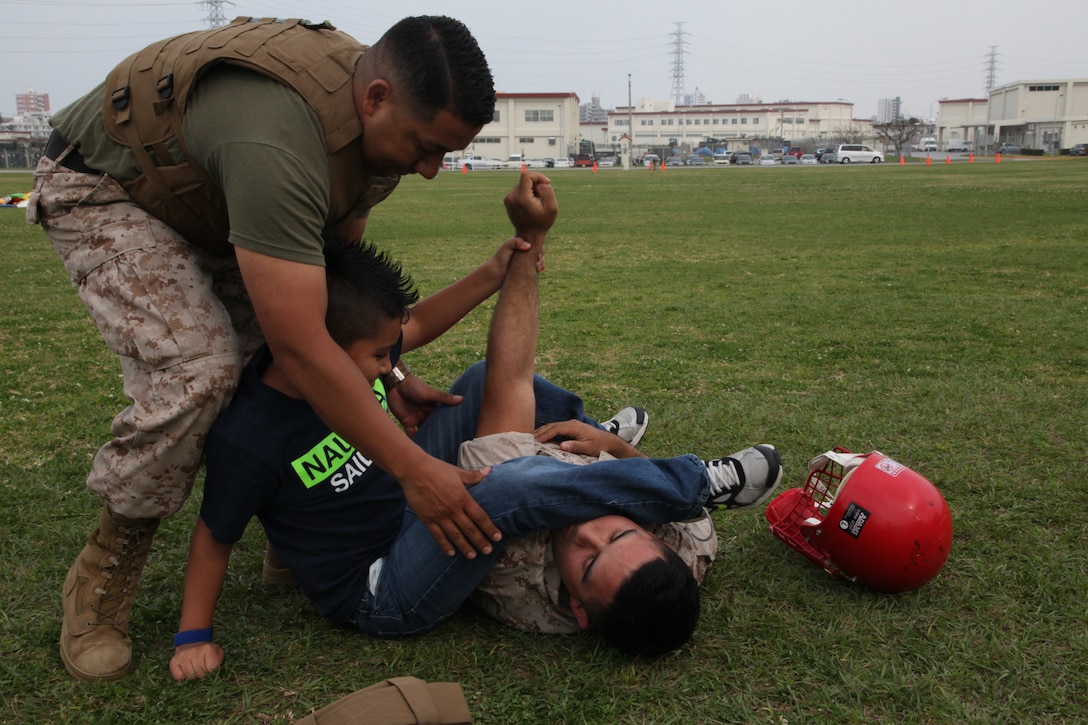 Staff Sgt. Jose A. Gonzalez, left, teaches Javier Ruiz how to execute an arm bar  at the parade deck on Camp Foster April 4 during a Junior Warrior Day. Teaching techniques associated with the Marine Corps Martial Arts Program were one of several activities children could participate in throughout the day. Gonzalez is a motor transport operations chief with Combat Logistics Battalion 4, Combat Logistics Regiment 3, 3rd Marine Logistics Group, III Marine Expeditionary Force, and Ruiz is a student of Zukeran Elementary. 