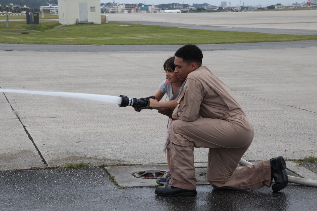 Lance Cpl. David D. EnriquezGonzalez helps Deanna Rohlf use a fire hose at the fire station on Marine Corps Air Station Futenma April 7during a visit from Girl Scouts. The goal was to use the hose to knock down a line of cones. The mission of Girl Scouts of America is to build the courage, confidence and character of girls, who can then make the world a better place, according to their website. EnriquezGonzalez is an aircraft rescue and firefighting specialist with ARFF, Headquarters and Headquarters Squadron, MCAS Futenma, Marine Corps Installations Pacific.