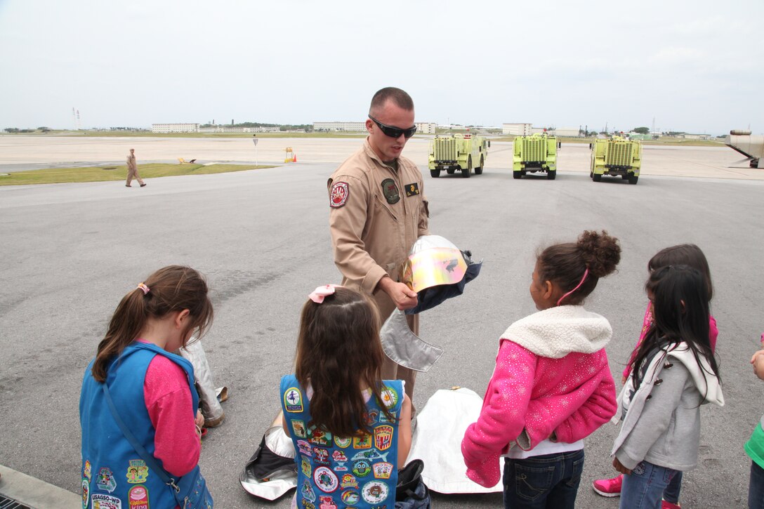 Lance Cpl. Jacob P. Sicard explains the purpose of a firefighter’s helmet at the fire station on Marine Corps Air Station Futenma April 7 during a visit from Girl Scouts. Marines with aircraft rescue and firefighting showed visiting Girl Scouts the equipment they use when responding to an emergency, such as the P-19A fire truck, proximity rescue suits they wear, and hydraulic tools that cut metal to assist in rescues. Sicard is an aircraft rescue and firefighting specialist with ARFF, Headquarters and Headquarters Squadron, MCAS Futenma, Marine Corps Installations Pacific. 