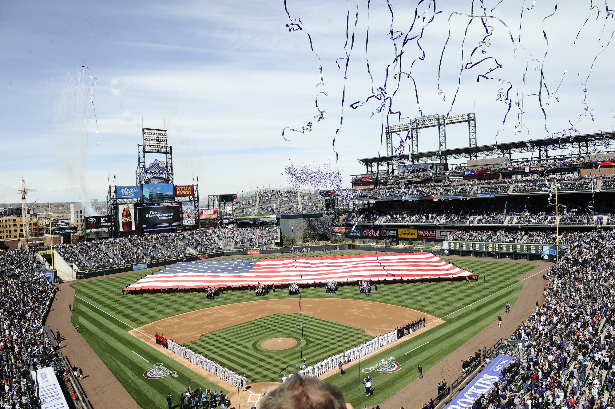 Colorado law enforcement officers and service members unfurl the American Flag while streamers and fireworks erupt during the Colorado Rockies Opening Day ceremony April 4, 2014, at Coors Field, Denver. Service members from all U.S. military branches stood in formations as local law enforcement and service members unfurled the American flag during the opening day ceremonies. (U.S. Air Force photo by Airman 1st Class Samantha Saulsbury/Released)