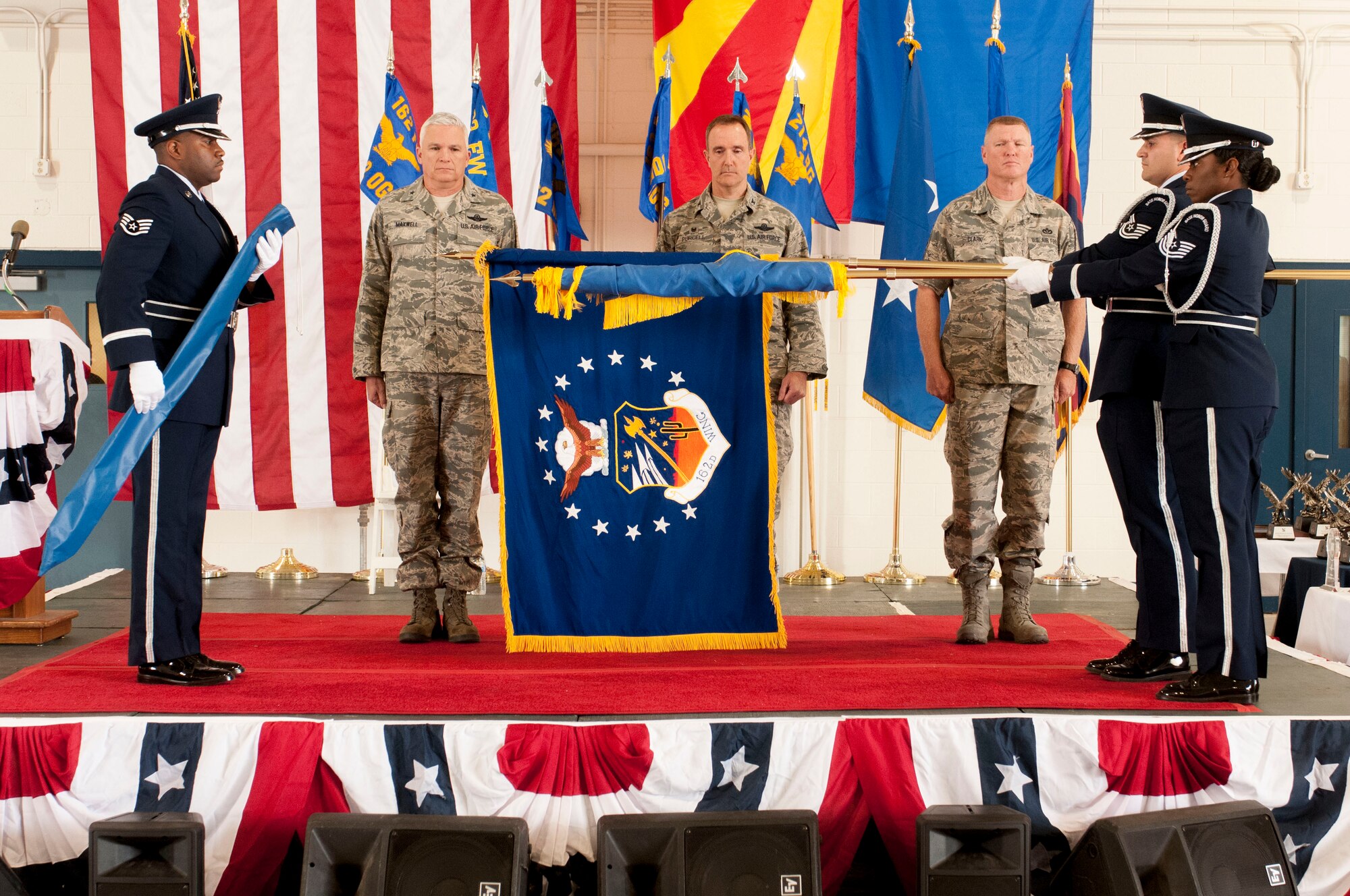 Out with the old, in with the new…a new wing name that is. The 162nd Fighter Wing is now the 162nd Wing, marking the official inclusion of the 214th Reconnaissance Group. Brig. Gen. Edward Maxwell, Commander of the Arizona Air National Guard, Col. Phil Purcell, the 162nd Wing Commander and Command Chief Master Sgt. Shane G. Clark, Chief Enlisted Advisor, witness the unfurling of the new 162nd Wing flag by Air National Guard Honor Guardsmen April 5 here at the Tucson International Airport. (U.S. Air National Guard photo by Tech. Sgt. Hollie Hansen)
