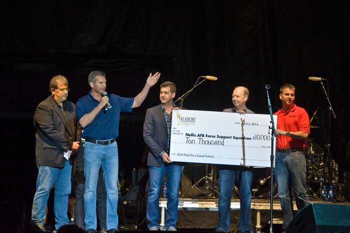 U.S. Air Force Col. Barry Cornish, 99th Air Base Wing commander, and Chief Master Sgt. Steven Cleveland, 99th ABW command chief, accept a check from Academy of Country Music at the ACM’s Party for a Cause festival April 5, 2014, in Las Vegas. The check was donated on behalf of the ACM’s Lifting Lives, the funds will be used for Nellis youth programs. (U.S. Air Force photo by Senior Airman Christopher Tam)