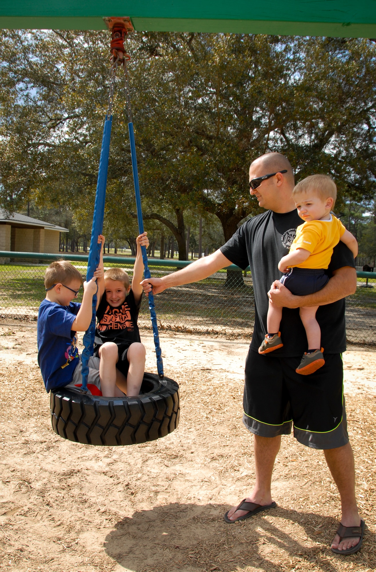Aiden and Ryan Lopardi, sons of Tech. Sgt. Chris Lopardi, of the 96th Civil Engineer Squadron Fire Department, enjoy a spin on the tire swing at Unity Park, as Chris and his son, Mason, look on.   The park reopened to the Eglin Air Force base community and their families April 1, following four months of renovations.  (U.S. Air Force photo/Kevin Gaddie)