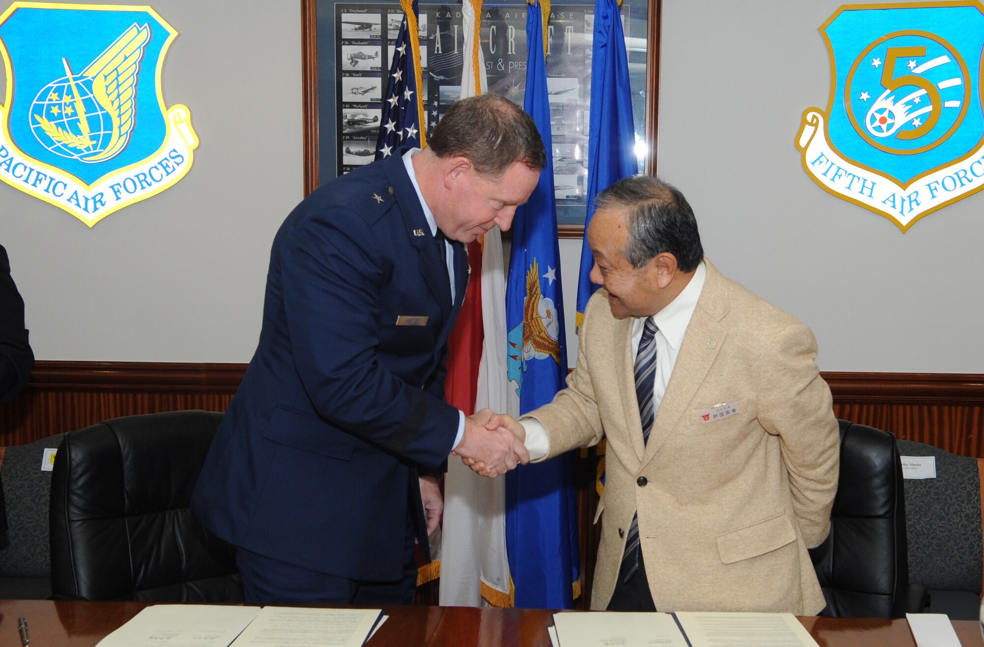 U.S. Air Force Brig. Gen. James Hecker, 18th Wing commander, and Masahau Noguni, mayor of Chatan City, shake hands after signing an official agreement which conveys an evacuation route Okinawan resident will utilize during a tsunami strike or in the event of a natural disaster on Kadena Air Base, Japan, April 3, 2014. As a part of the agreement, the United States Air Force will provide a route that runs through Kadena Air Base to Okinawa City where higher ground is located due to much of Chatan City lying in a low coastal area, with limited options to moving residents to the safety of higher ground. (U.S. Air Force photo by Airman 1st Class Keith James)