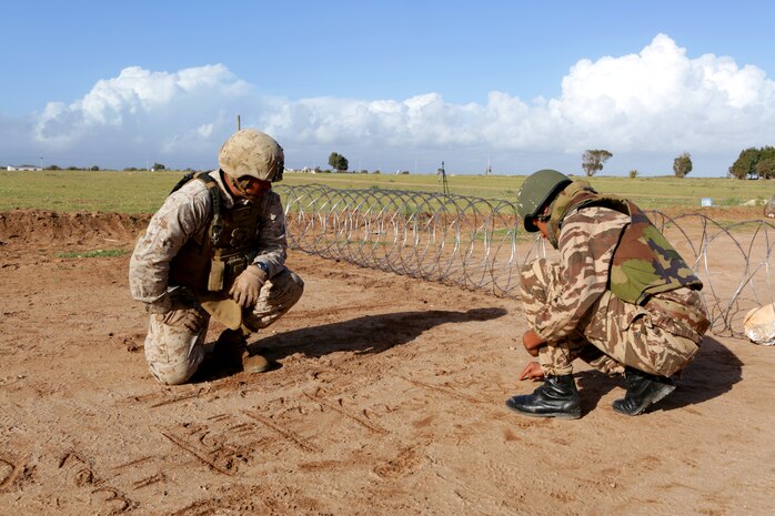 A Moroccan soldier and Lance Cpl. Michael A. Laureano, a Brentwood, N.Y., native and military policeman with 2nd Law Enforcement Battalion, share and show military grades and ranks from their respective countries as they draw them out in the sand during Exercise African Lion 14. Military police officers from the U.S. Marines, Army and Air Force, along with Royal Moroccan soldiers specializing in riot-control, found common ground as enforcers of the law during African Lion 14, an annually-scheduled, multilateral training engagement that is hosted by the Kingdom of Morocco. One of the largest of its kind on the continent, the engagement shows the commitment of the participating nations to military friendships, strategic partnerships and regional and global security. 