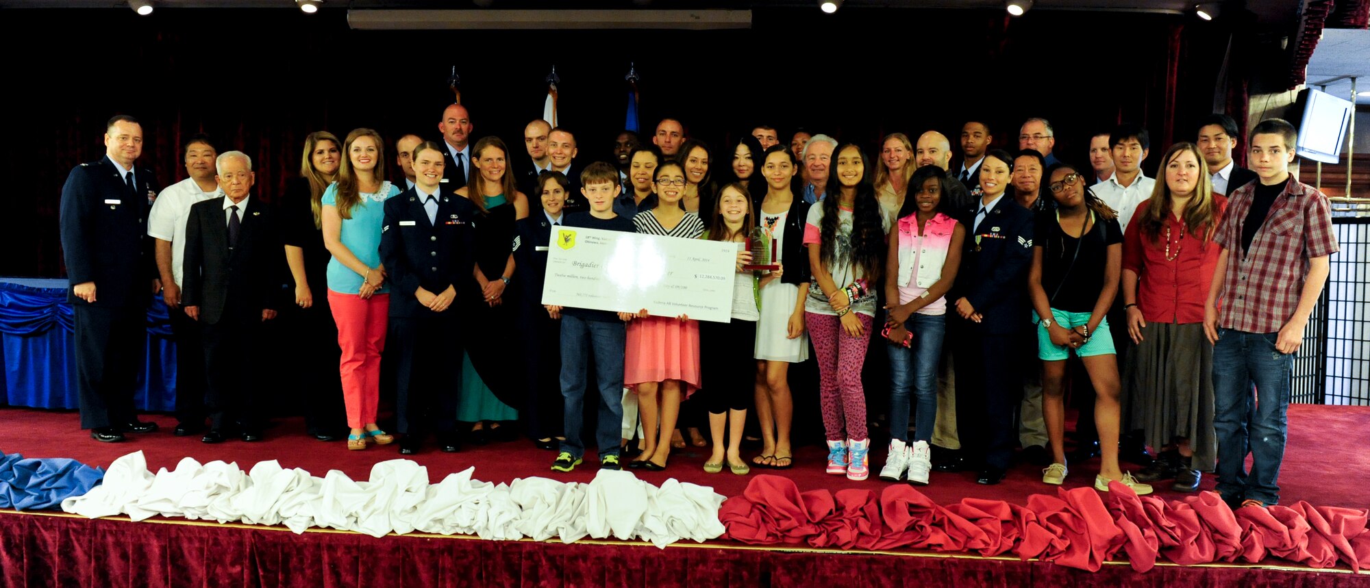 Volunteers honored in a recognition ceremony on Kadena Air Base, Japan, hold up a check representing the minimum wage amount they collectively saved the Air Force during the event April 11, 2014. The more than 30 volunteers worked a collective 563,771 hours in the Kadena community. In terms of minimum wage, the volunteers saved the Air Force a total of more than $12.8 million. (U.S. Air Force photo by Senior Airman Maeson L. Elleman)
