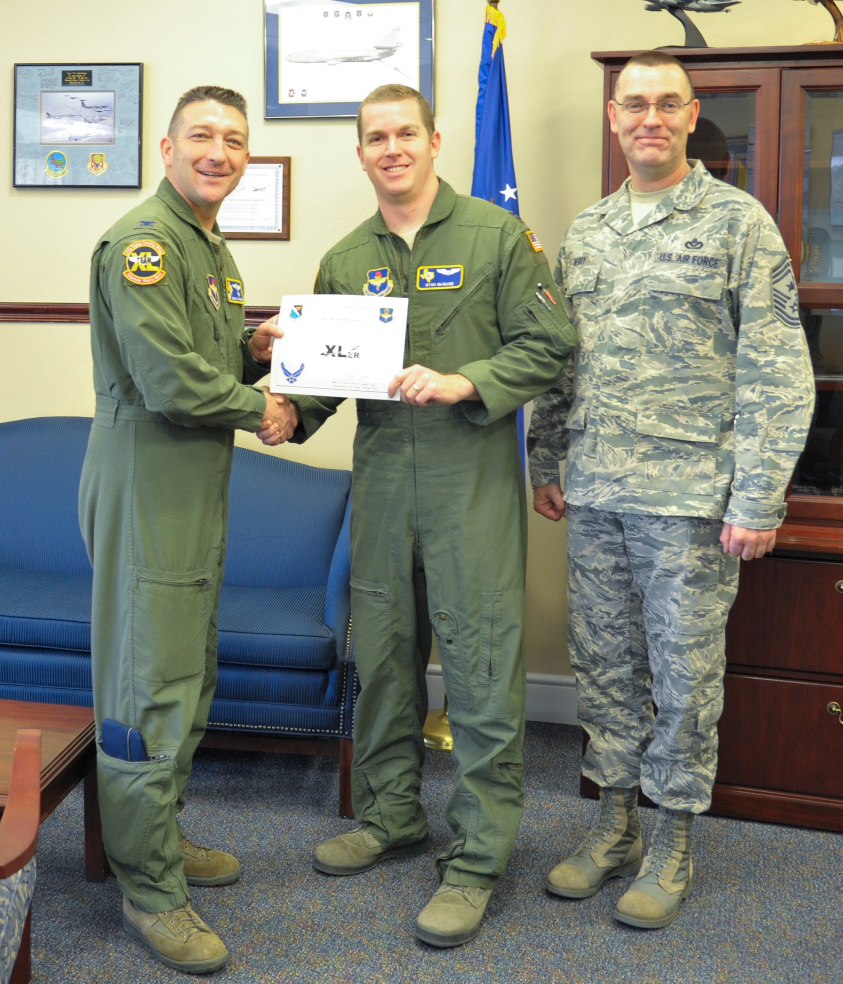 Capt. Ryan McGuire, center, 47th Operations Group executive officer and T-1A Jayhawk instructor pilot, poses with Col. Brian Hastings, left, 47th Flying Training Wing commander, and Chief Master Sgt. Garry Berry, right, 47th FTW command chief, after being presented the XLer of the week award here April 9, 2014. The XLer is a weekly award chosen by wing leadership and given to those who consistently make outstanding contributions to their unit and Laughlin. (U.S. Air Force photo/Airman 1st Class Jimmie D. Pike/Released)