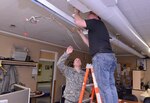 A civilian contract electrician works to replace old lighting fixtures with newer, more energy efficient lighting at the Cottage Grove armory, Feb. 20, 2014. It's part of the challenge to save energy.