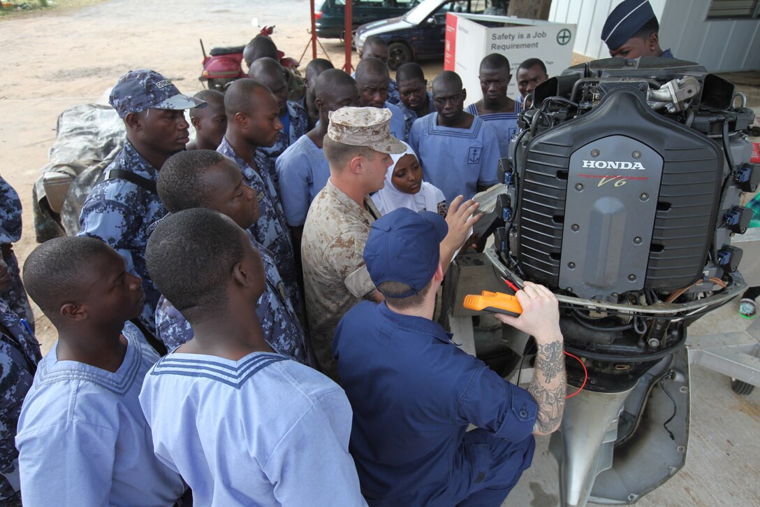 A group of sailors with the Togolese Navy watch as Lance Cpl. Tyler Jackson, a Marine with Special-Purpose Marine Air-Ground Task Force Africa 14.1, and Petty Officer 3rd Class Brian Spence, a Coastguardsman with U.S. Coast Guard Station Seattle, discuss small-boat engine mechanics in Lomé, Togo, March 25. Jackson and Spence put together a week-long training program of classroom instruction and practical application so the two groups of service members could partner together to fix engines. Established in 2011, Special-Purpose Marine Air-Ground Task Force Africa 14.1 is charged with supporting U.S. Africa Command and Marine Corps Forces Europe and Africa’s theater security cooperation requirements.