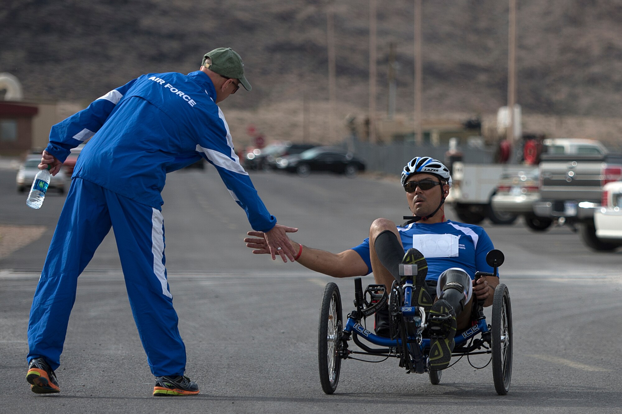 Christopher Aguilera cycles by Mike Sanders to receive a high-five after he finished the race April 9, 2014, during the Air Force Trials at Nellis Air Force Base, Nev. Aguilera, and Air Force wounded warrior, placed first in his category during the cycling completion. (U.S. Air Force photo/Senior Airman Jette Carr)