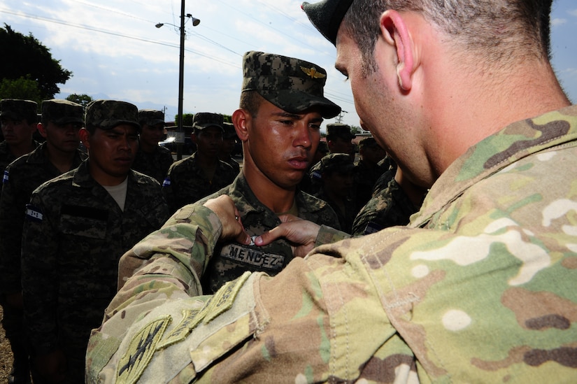 A 7th Special Forces Group paratrooper pins a set of jump wings on a Honduran 2nd Combat Airborne Infantry Battalion paratrooper during a wing exchange after performing joint airborne operations training consisting of jumping from a C-130 Hercules aircraft at Soto Cano Air Base, Honduras on April 3, 2014.  The 1,500 foot static line jump allowed members from both nations to retain currency, while also strengthening the relationship between the U.S. and Honduran forces.  (Photo by Martin Chahin)